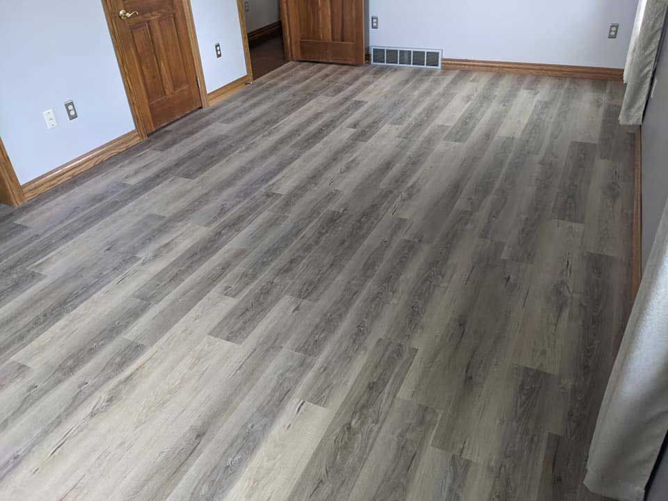 Gray wood-look flooring in a room with two wooden doors, light walls, and a window.
