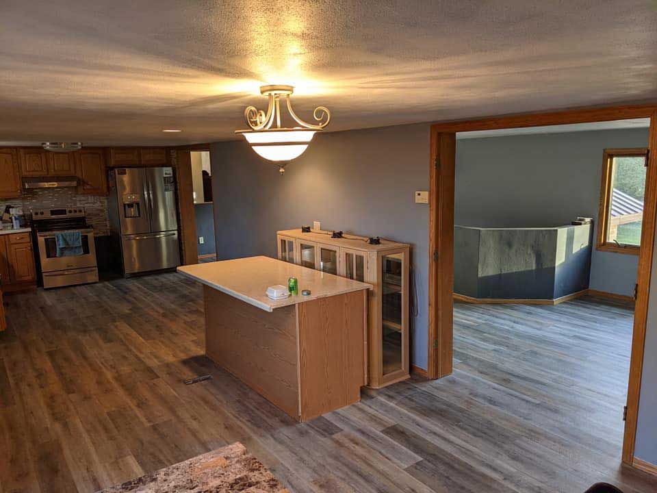 Kitchen with wood flooring, unfinished island, gray walls, and open doorway to another room.