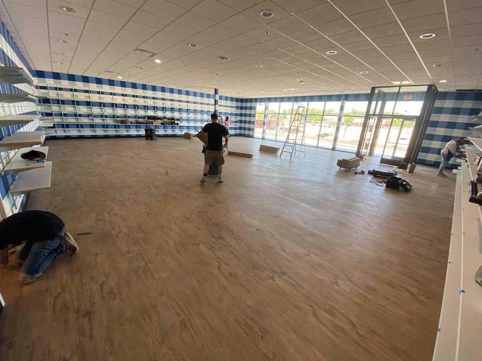 Workers install flooring in a large retail space with blue and white checkered wall and shelving.