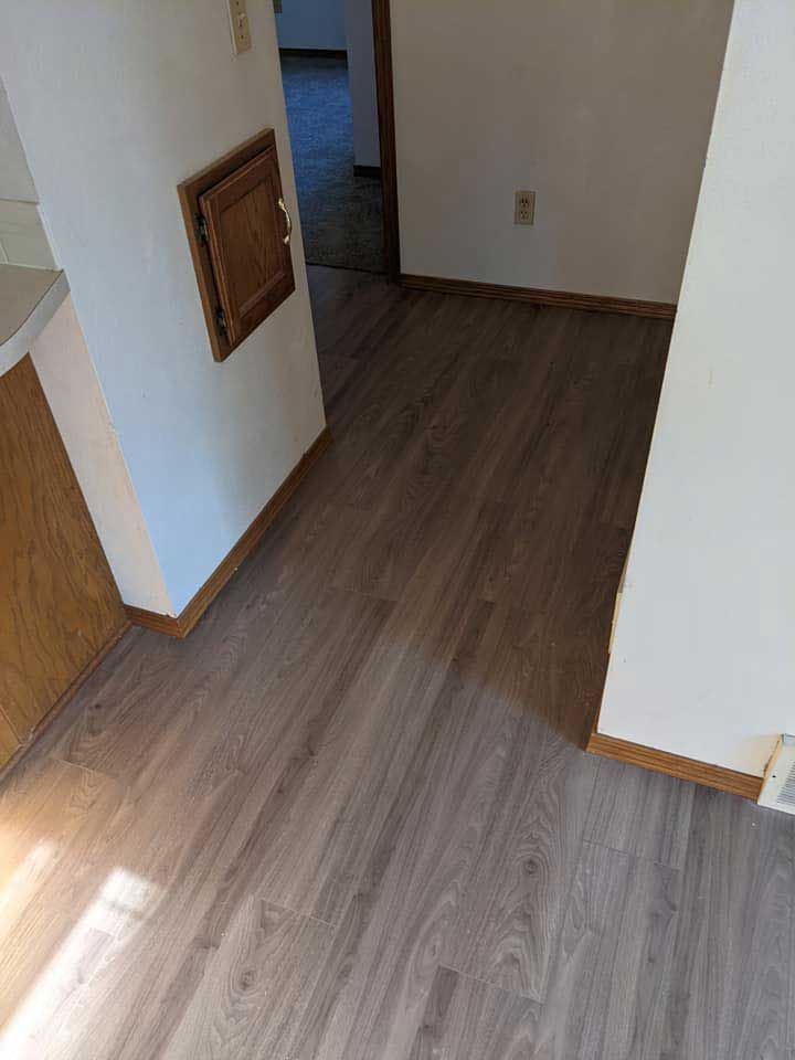 Hallway with wood-look flooring and white walls. A small wooden door and an electrical outlet are visible.