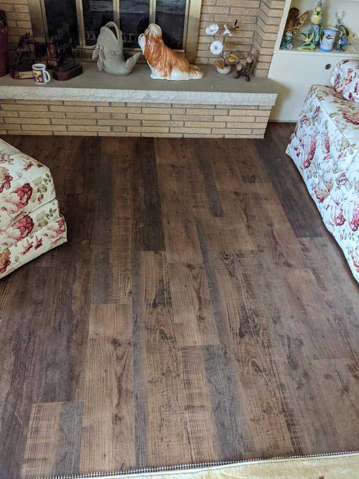 Dark wood-look flooring in a living room, with a brick hearth and floral furniture visible.