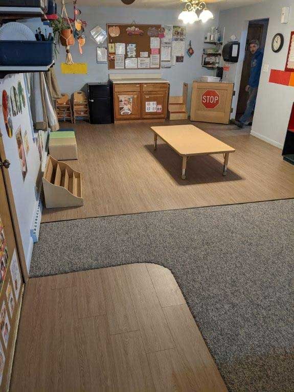 Interior of a room with hardwood and carpet floors, a low table, and cabinets. A person stands in the doorway.