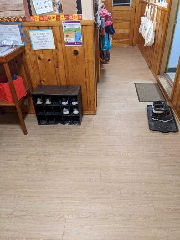 Hallway with wooden walls, shoe rack, and light wood flooring.