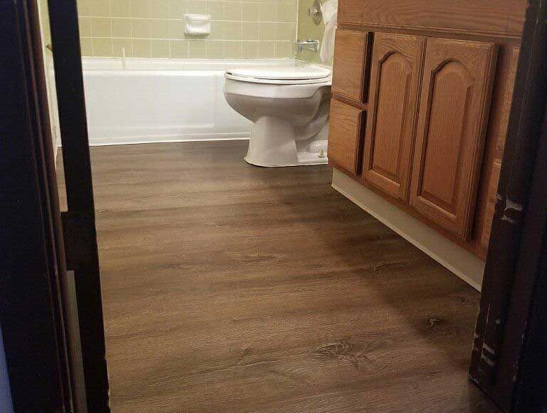 Bathroom interior with brown floor, white toilet and tub, and wood vanity.