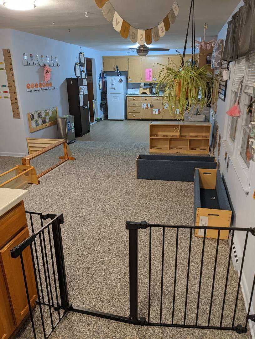 Indoor playroom with safety gates, carpet, and storage. Kitchen visible in the background.