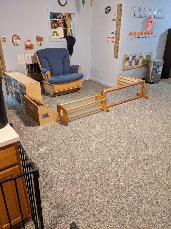 A child's playroom with wooden furniture, a blue rocking chair, and a light-colored carpet.