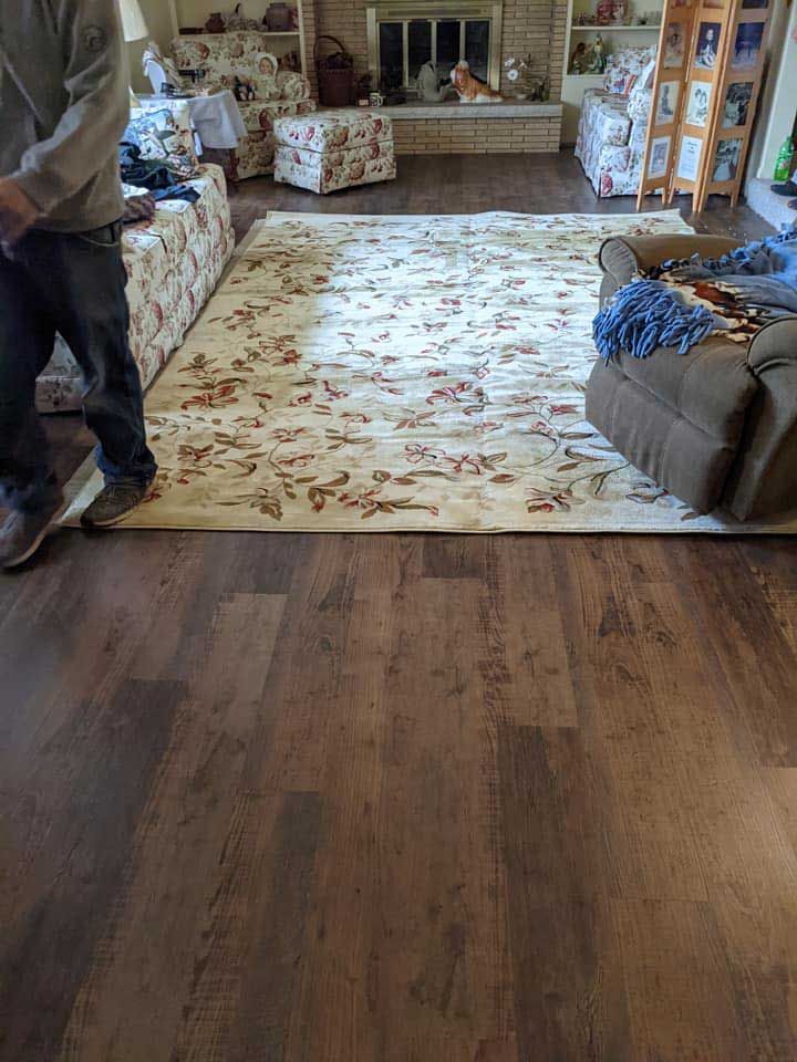 Person standing near a rug and furniture in a living room with wood flooring, and a fireplace in the background.