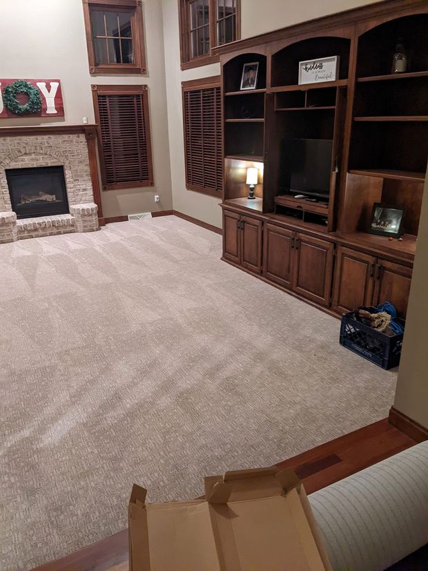 Living room with tan carpet, built-in wooden entertainment center, and fireplace with stone.