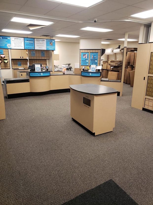 Interior of a shipping store with counters, cardboard boxes, and a central display table on patterned carpet.
