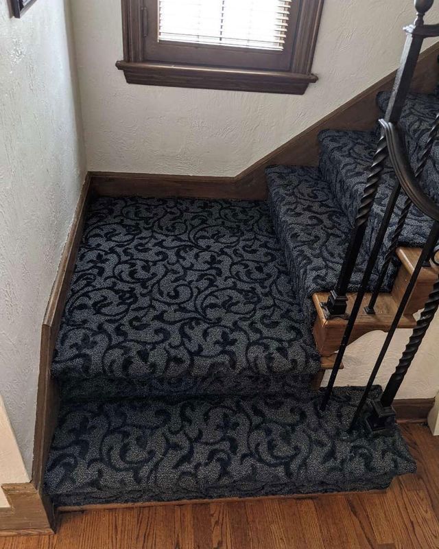 Staircase with patterned dark gray carpet and a dark wooden railing.