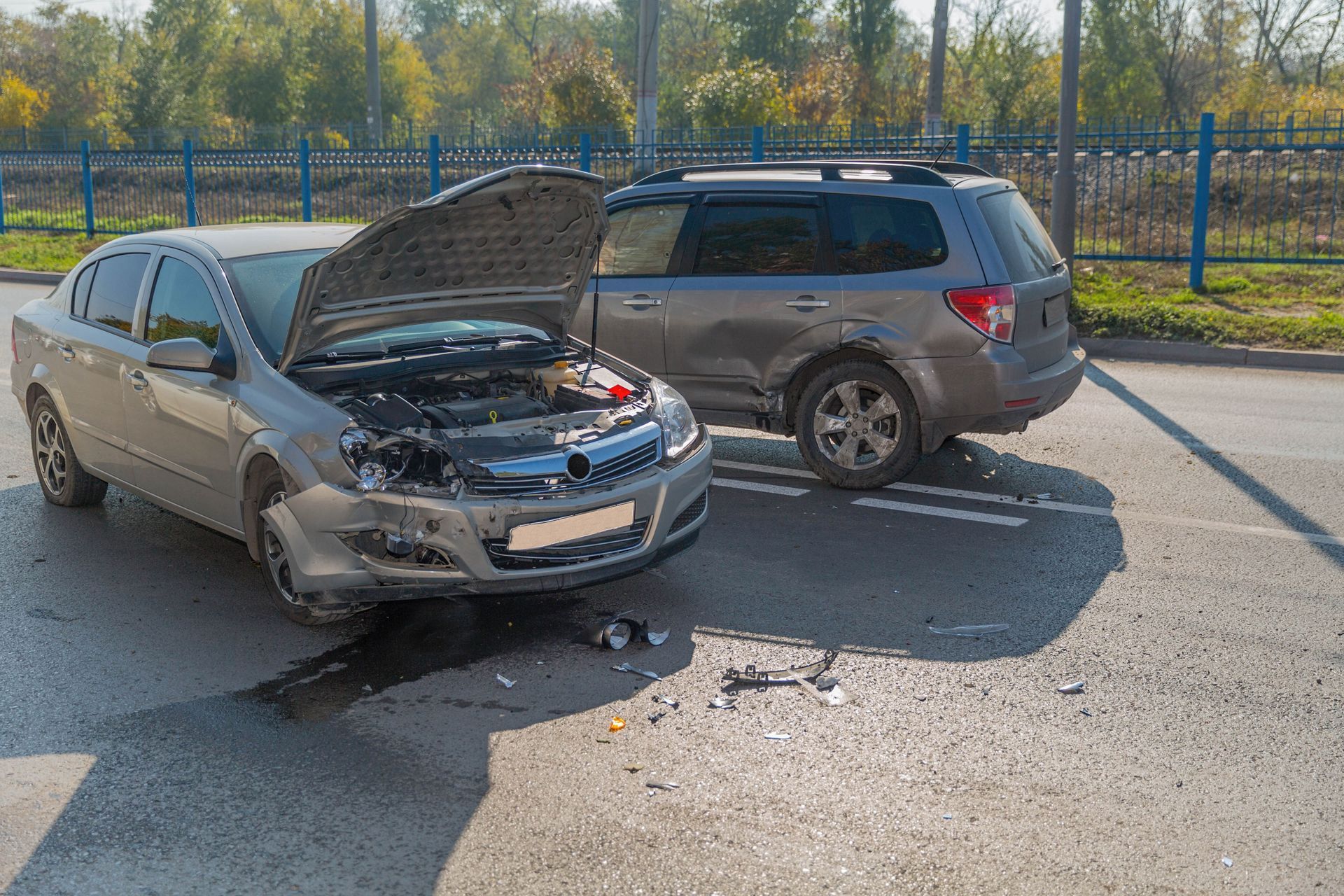 Two damaged cars after a collision on a road. One car's hood is open, debris scattered.