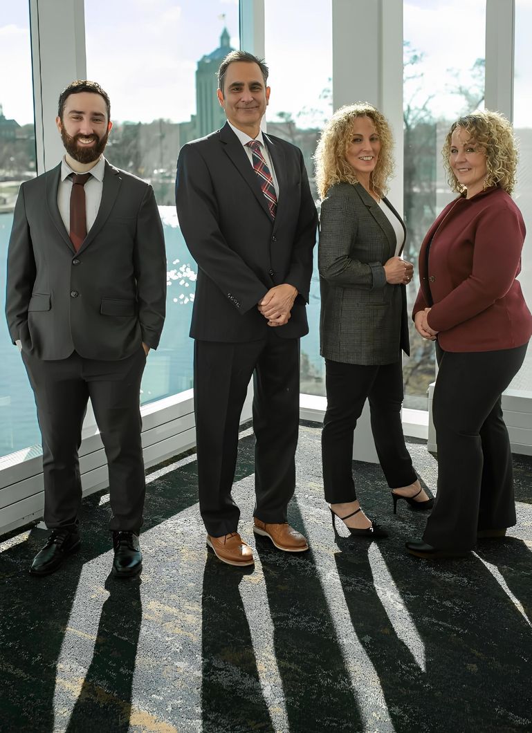 Four professionals pose near a window. Two men in suits and two women in business attire, smiling.