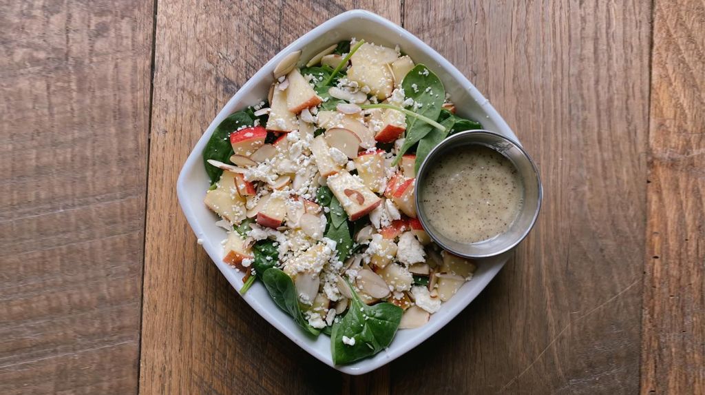 A bowl of salad with a spoonful of dressing on a wooden table.