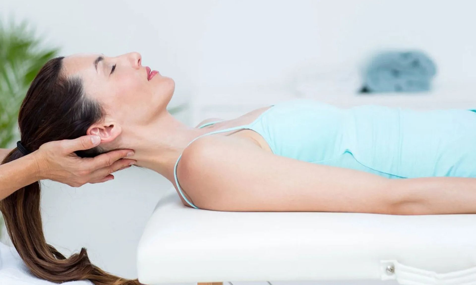 Woman lying on a massage table while a therapist supports her head and neck
