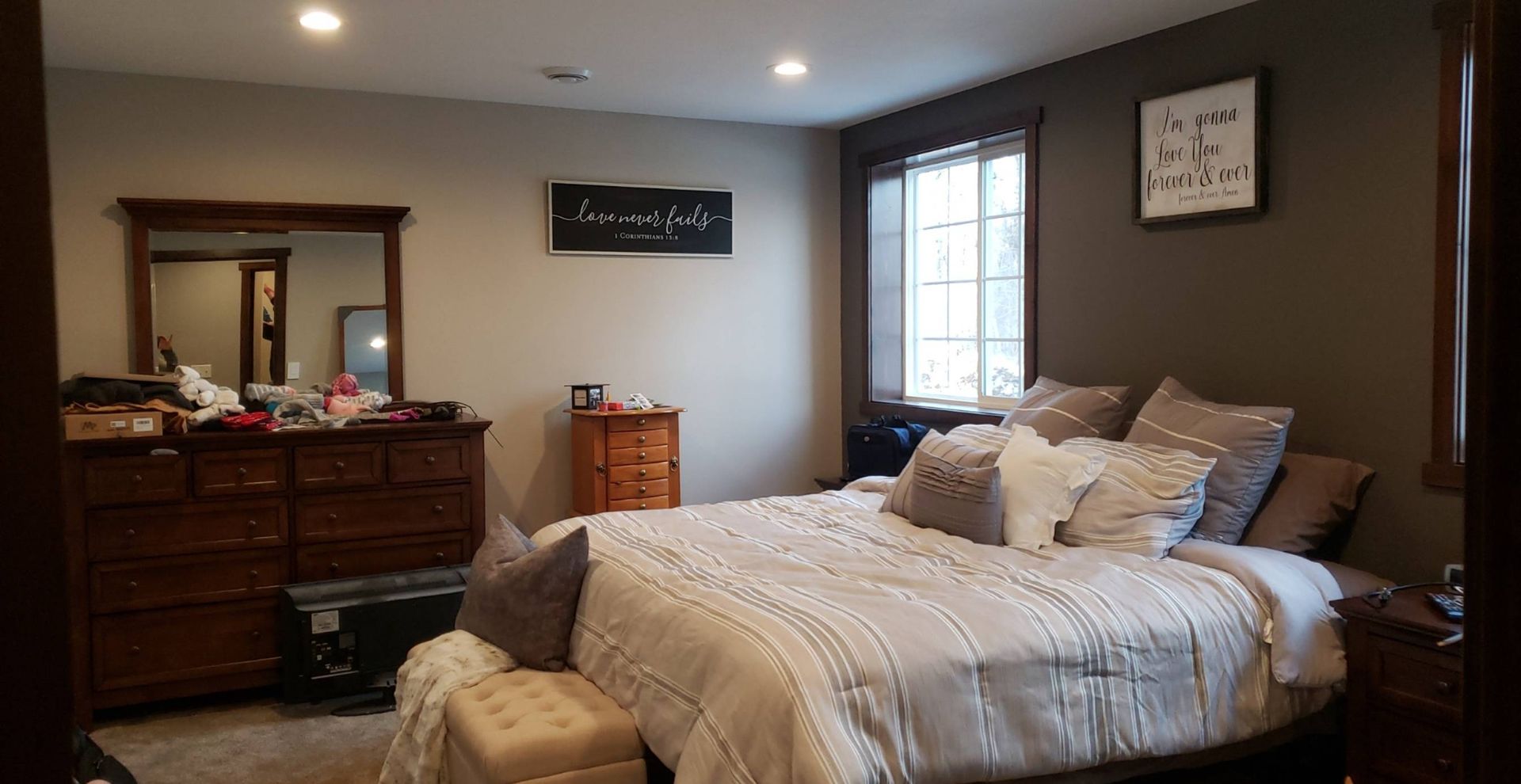A bedroom with a large bed , dresser , mirror and window.