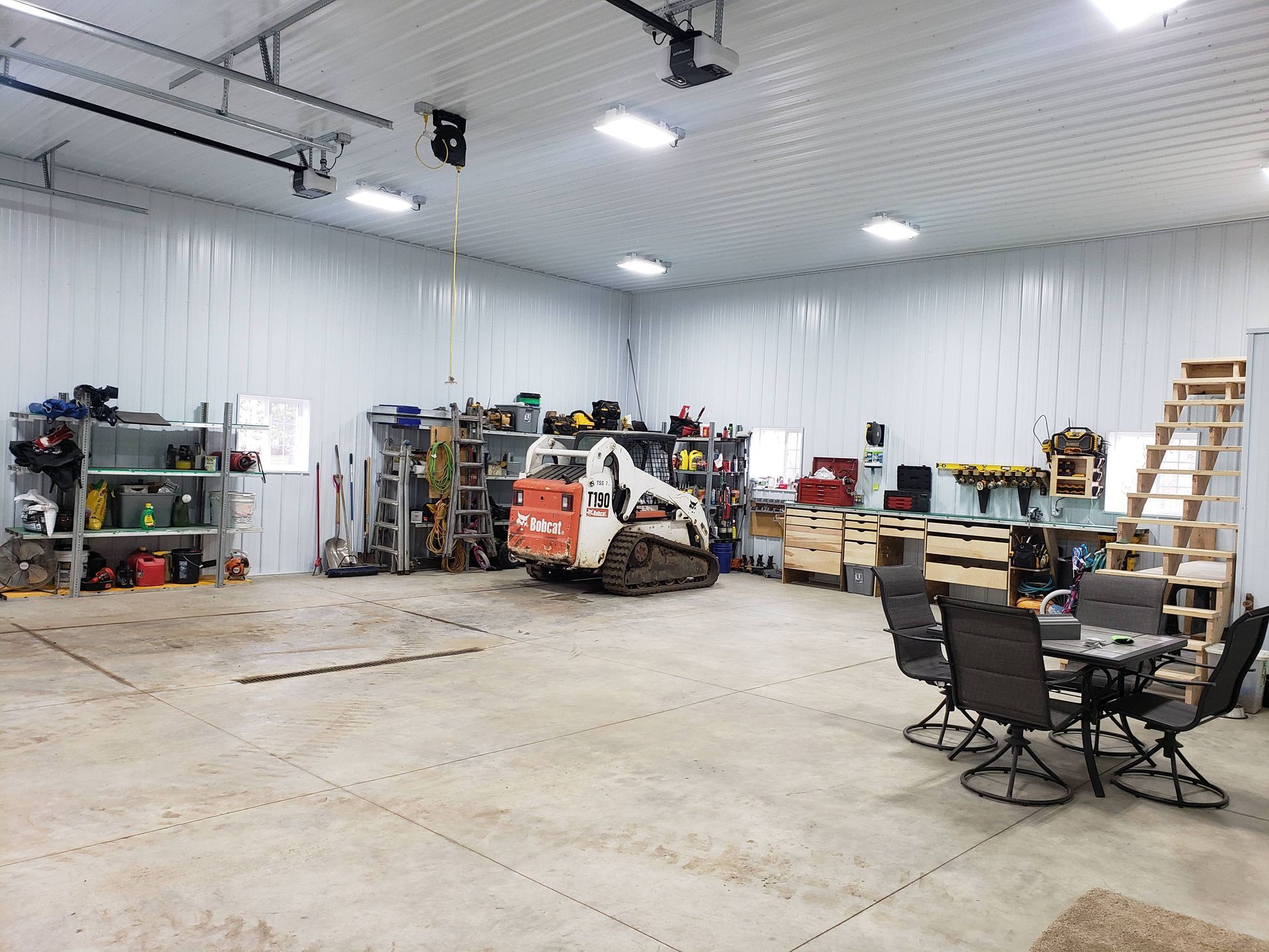 A bobcat is parked in a garage next to a table and chairs.