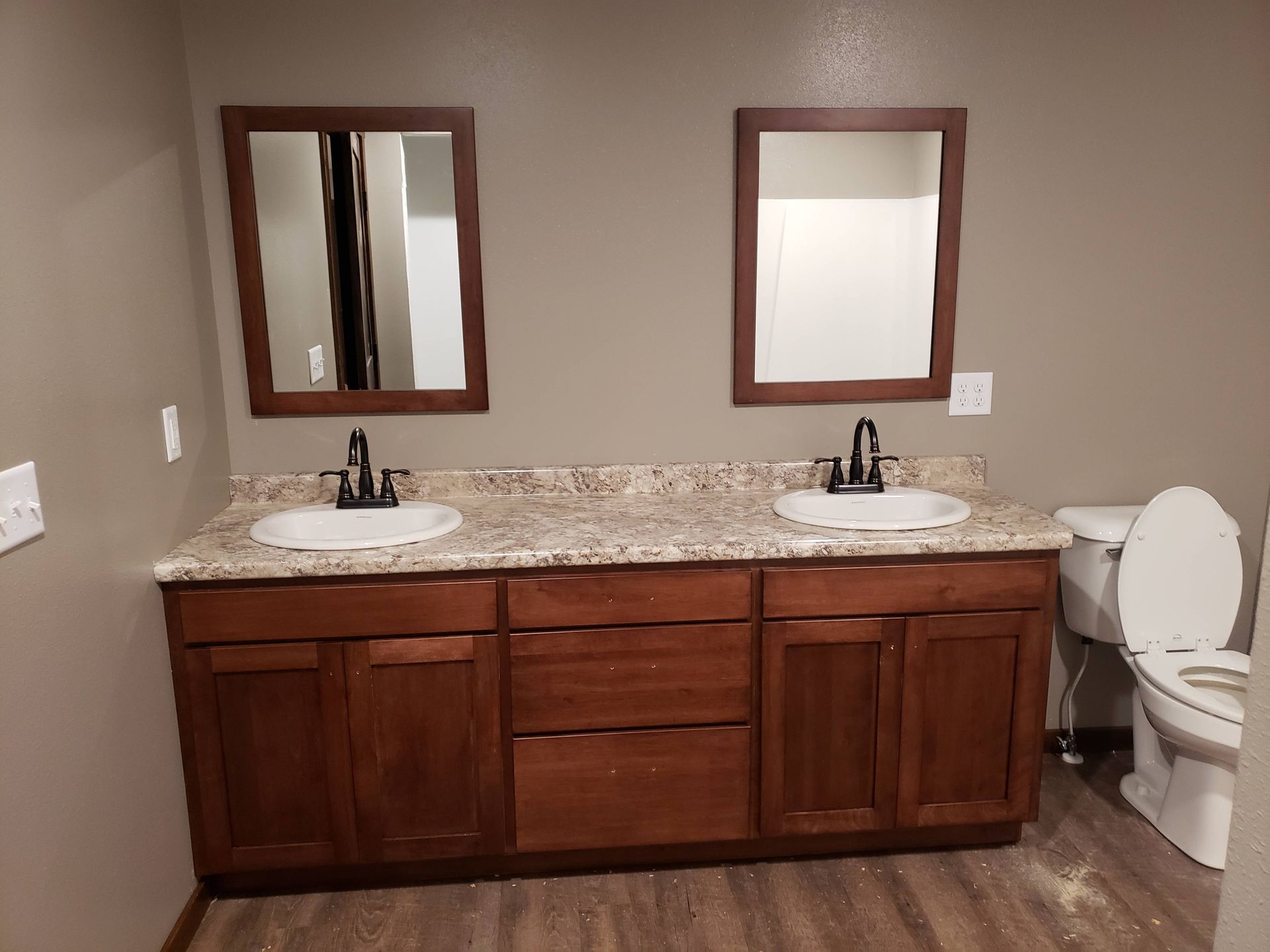 A bathroom with two sinks , two mirrors and a toilet.