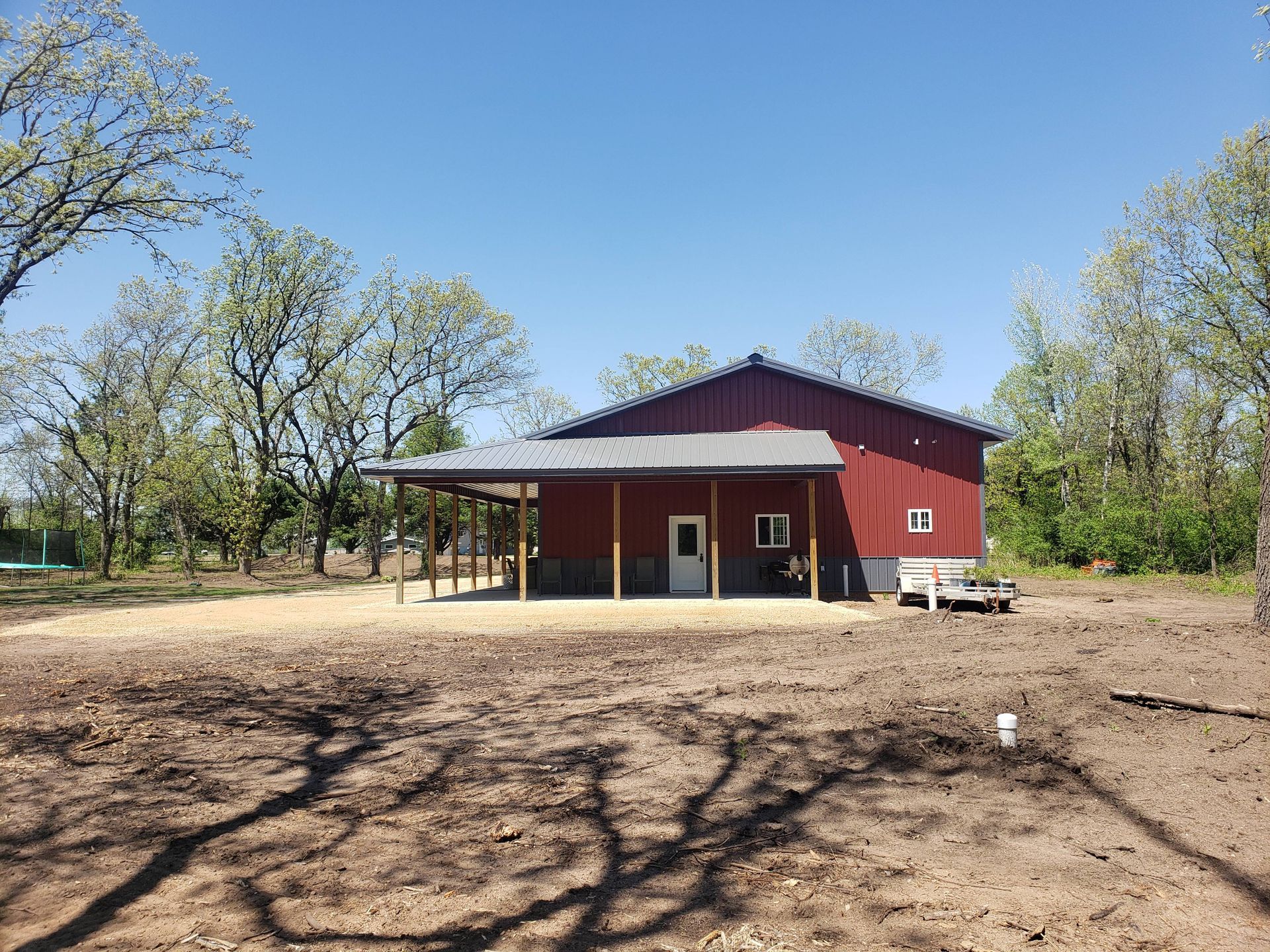 A red barn with a porch is sitting in the middle of a dirt field.