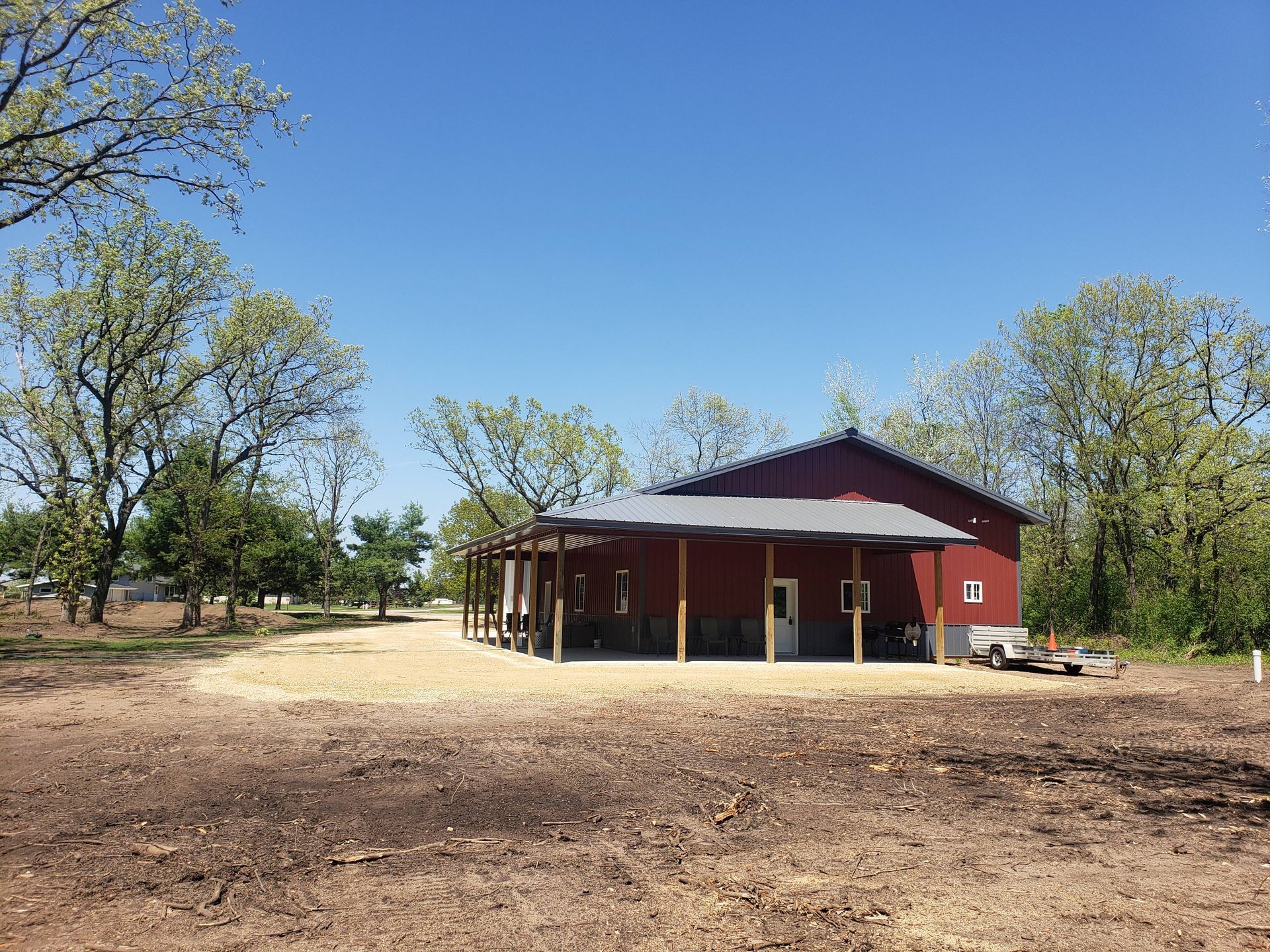 A red barn is sitting in the middle of a dirt field surrounded by trees.