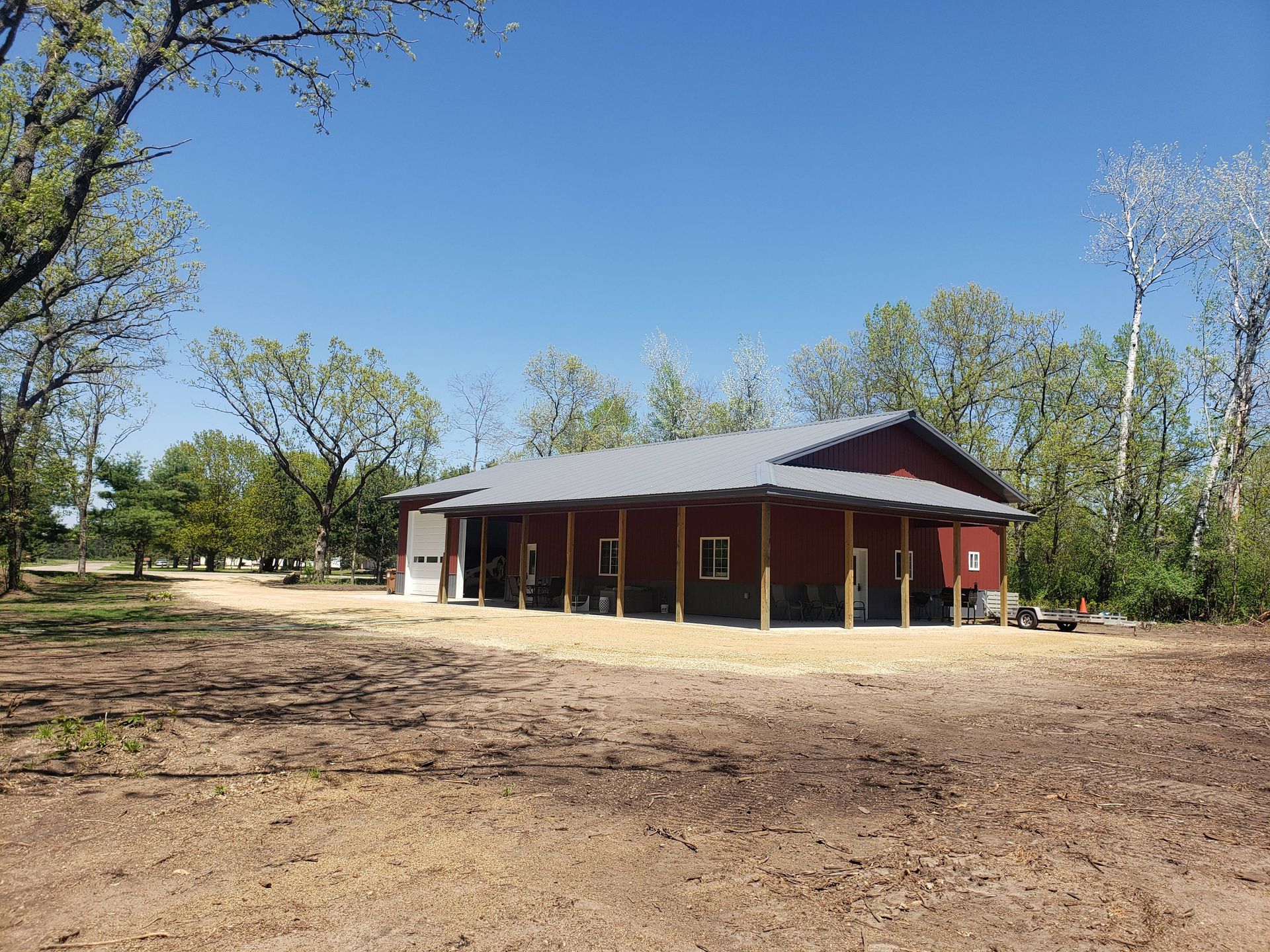 A large red barn is sitting in the middle of a dirt field surrounded by trees.