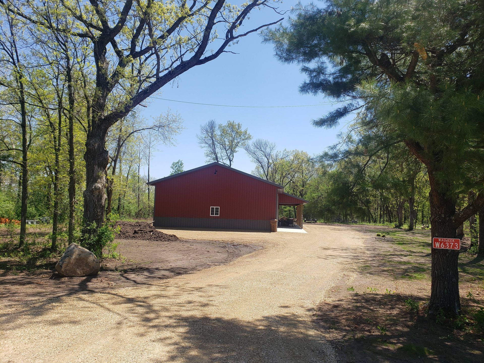 A red barn is sitting in the middle of a dirt road surrounded by trees.