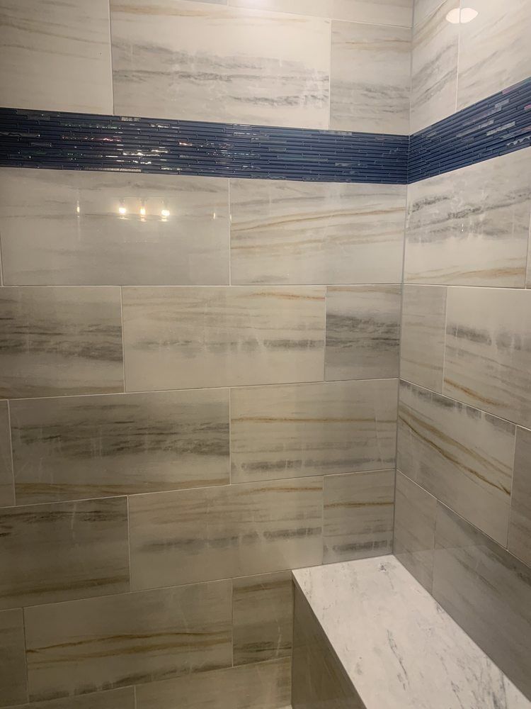 Tiled shower corner with gray wood-look walls and a blue accent band, plus a built-in bench