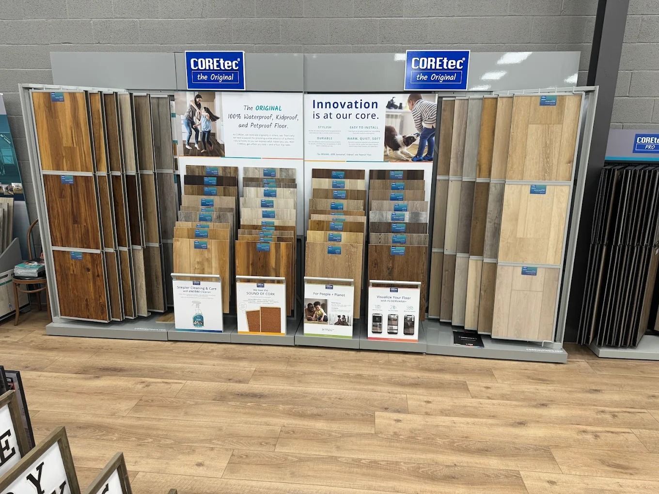 Display of vinyl flooring samples in a home improvement store, with wood-look planks and signs above.