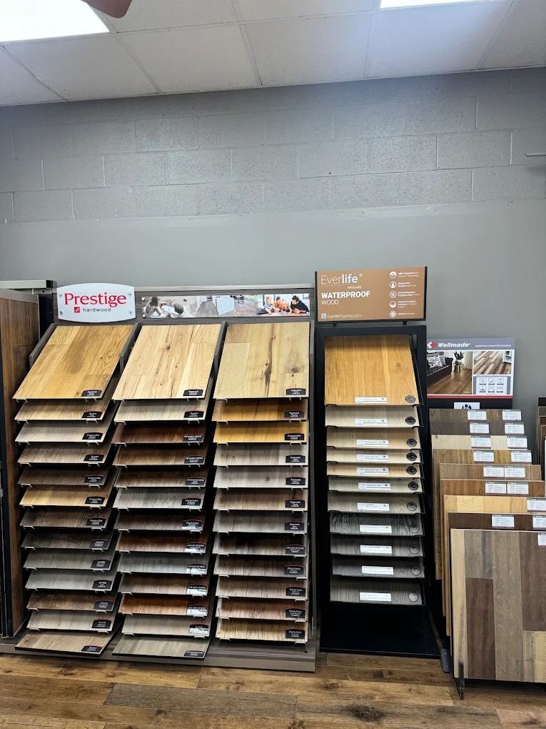 Display of wood and laminate flooring samples in a showroom against a gray wall