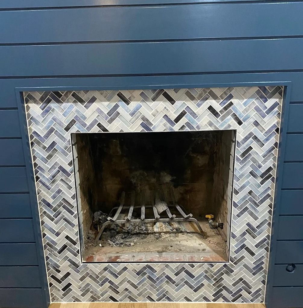 Empty outdoor fireplace with a blue wood siding wall and patterned mosaic tile surround