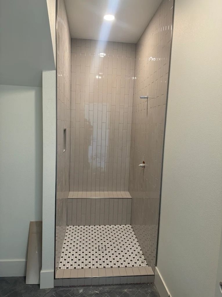 Glass walk-in shower with white mosaic floor and light tiled wall in a bathroom.