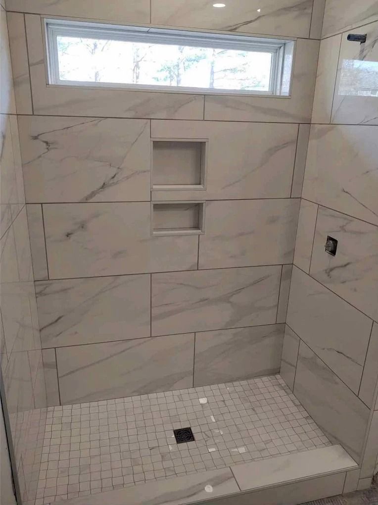 Tiled walk-in shower with built-in shelves, a small window, and a tiled bench with a floor drain.