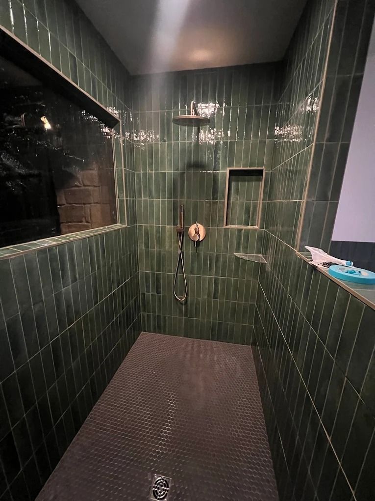 Empty dark green tiled shower stall with a floor drain and wall-mounted controls