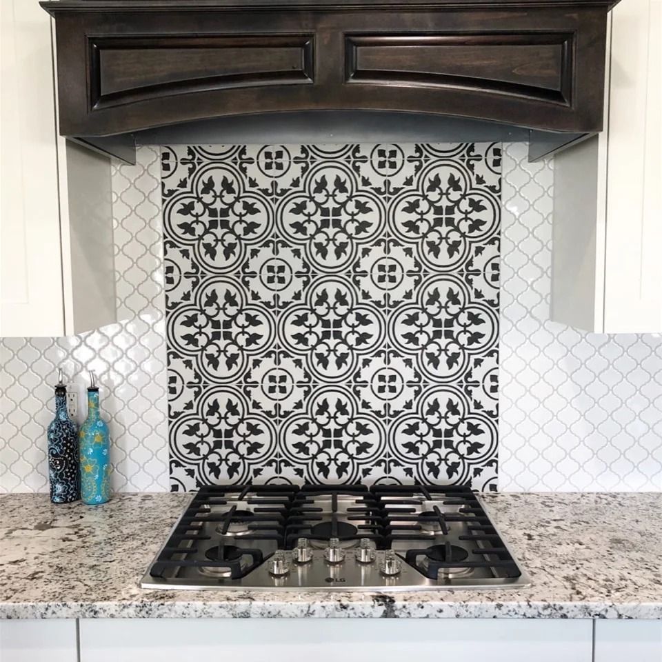 Kitchen stove with granite countertop, black-and-white patterned tile backsplash, and dark wood range hood