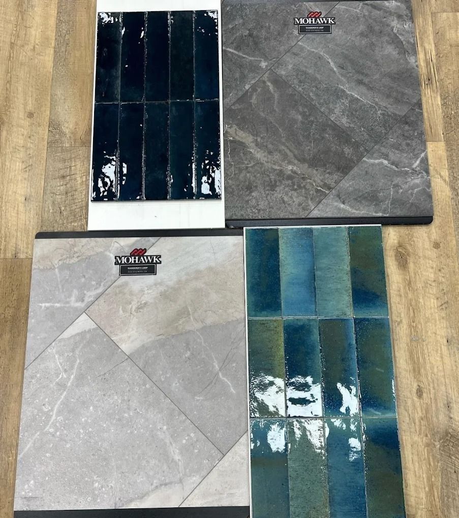Four decorative tile samples in gray, black, and blue-green laid out on a wooden surface