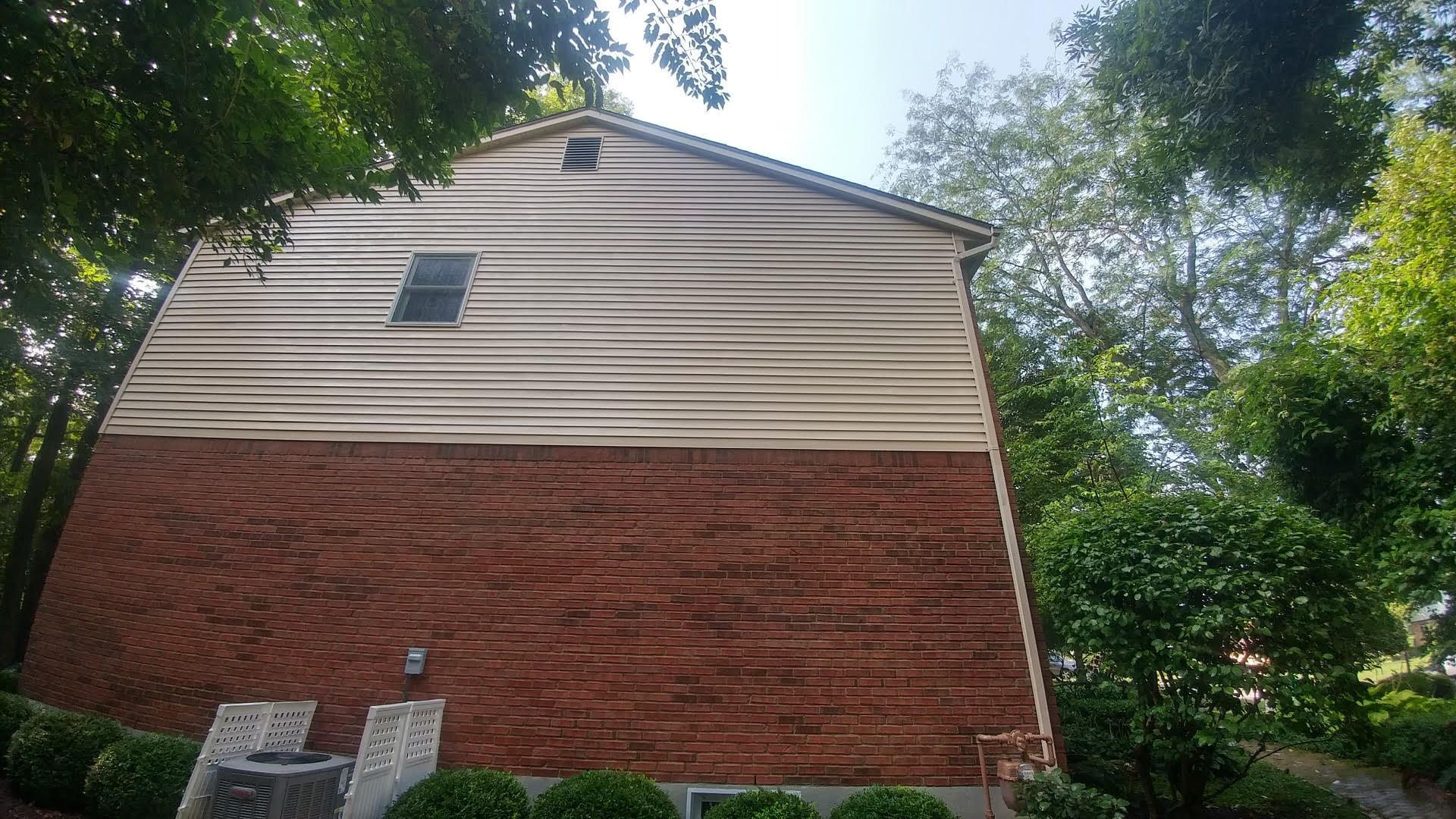 A large brick house with a white siding is surrounded by trees.