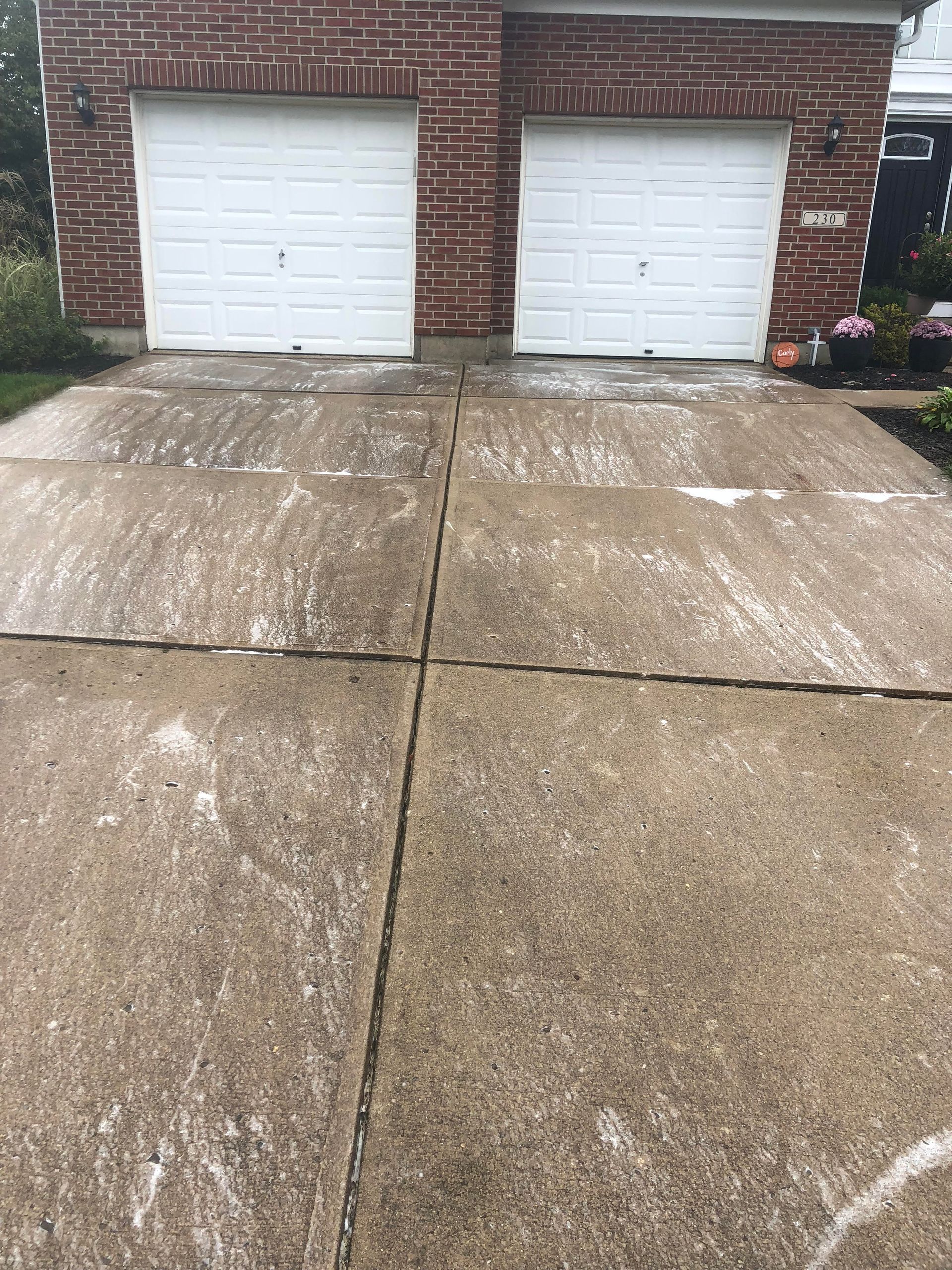 A concrete driveway in front of a brick house with two garage doors.