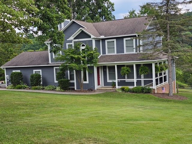 Two-story blue house with white trim, a porch, and a green lawn. Trees surround the house.