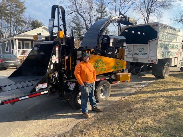 Man stands by wood chipper and truck; tree service equipment.