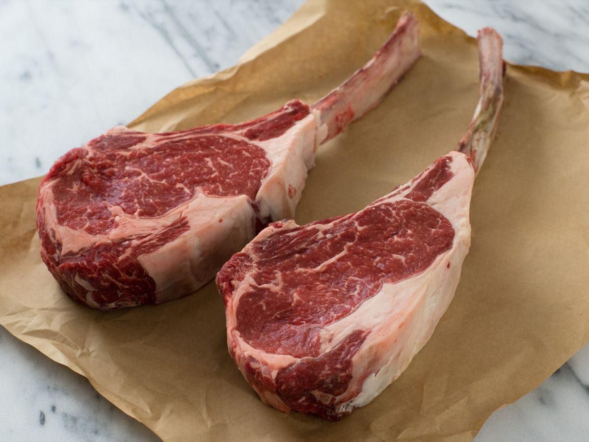 Two raw lamb chops are sitting on a piece of brown paper.