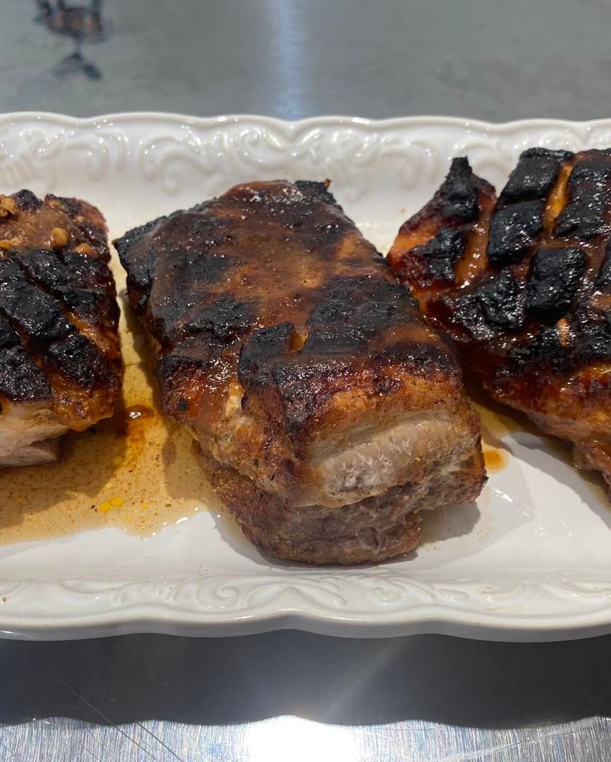 Three pieces of meat are on a white plate on a table.