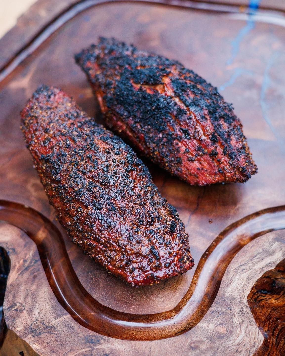 Two pieces of meat are sitting on a wooden cutting board.