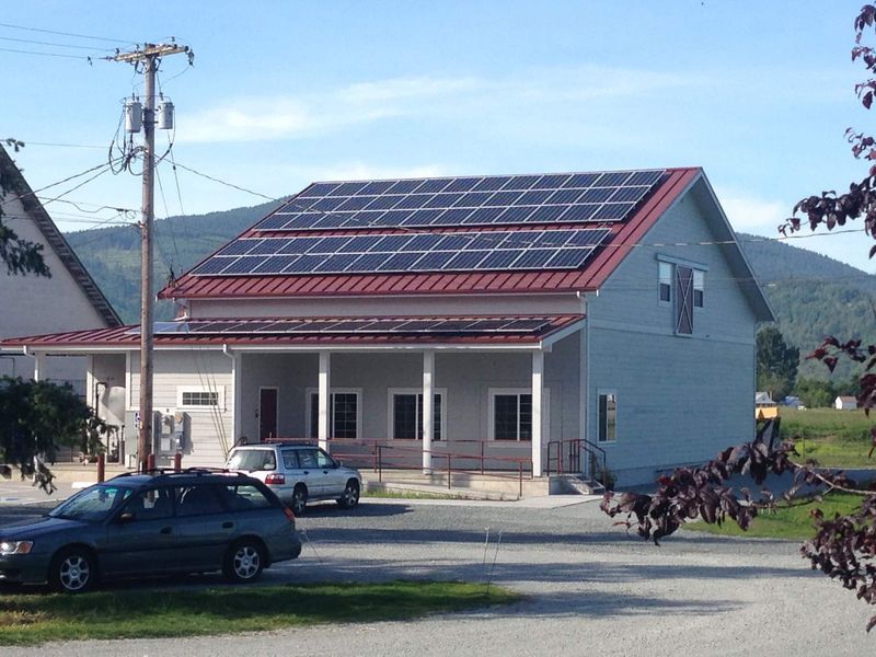 Building with solar panels on roof, cars parked outside, clear sky.