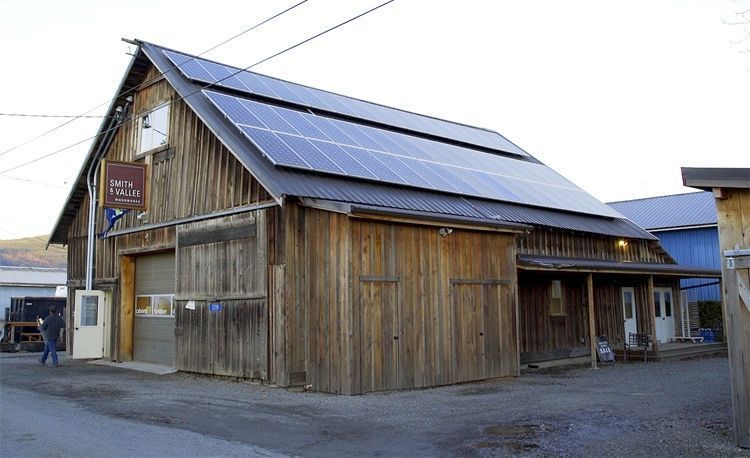 Wooden barn with solar panels on the roof; storefront entry and garage door. A person walks near the entrance.