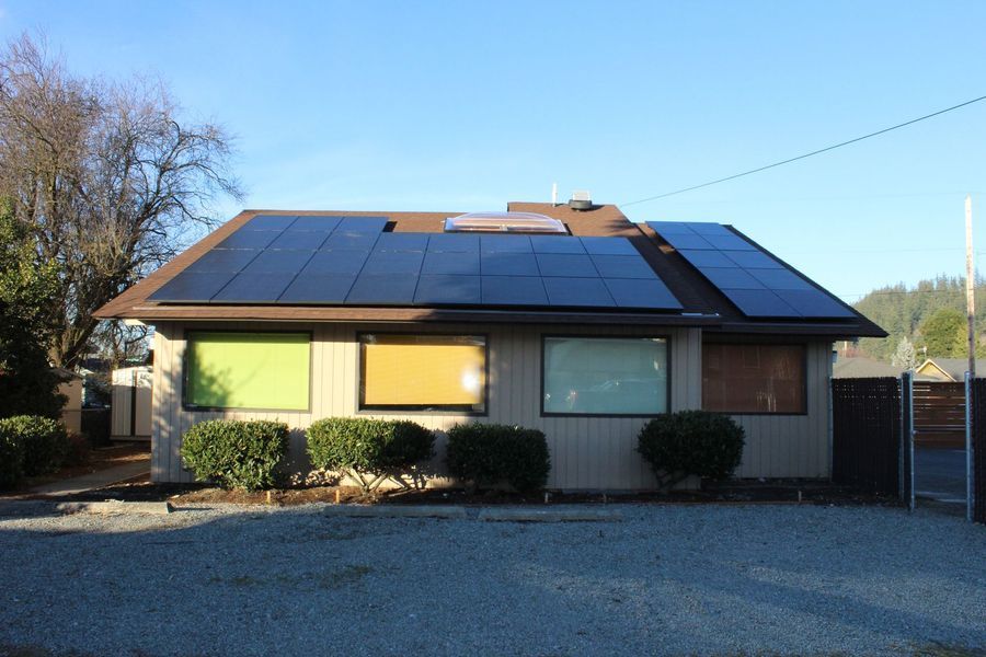 Beige house with solar panels on roof, windows with colorful light, and bushes.