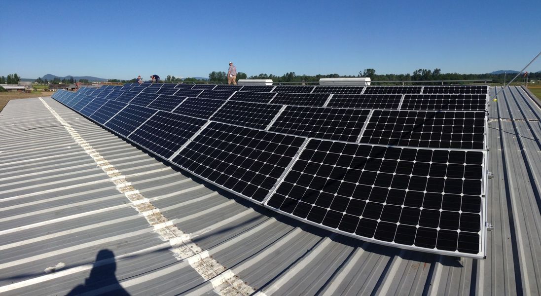 Solar panels installed on a corrugated metal roof under a blue sky.