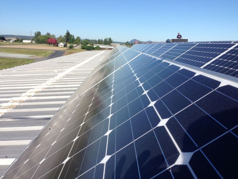 Solar panels on a building roof, reflecting the sky. In the background: buildings and fields.
