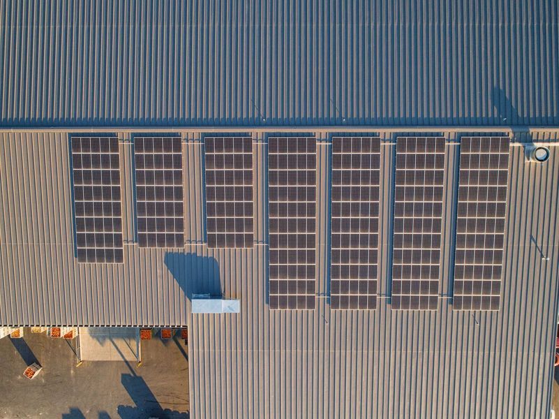 Overhead view of a metal roof with six rectangular solar panels installed on it.