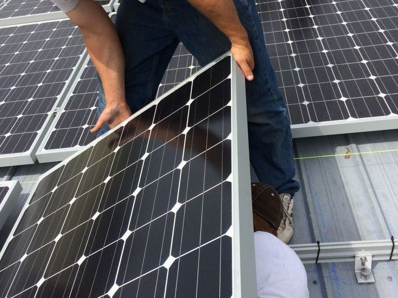 Workers installing a solar panel on a rooftop.