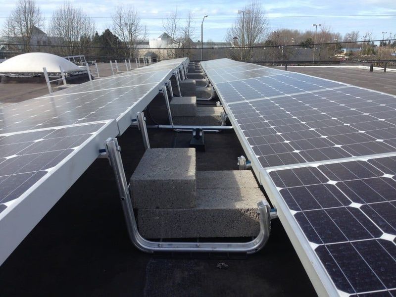 Solar panels installed on a flat roof, arranged in rows with supporting structures and concrete blocks.