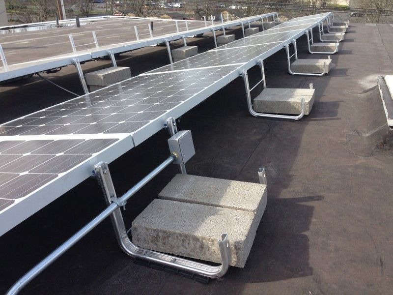 Solar panels installed on a flat roof, elevated by metal frames and weighted with concrete blocks.